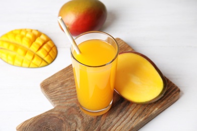 Glass with fresh mango juice and tasty fruits on table