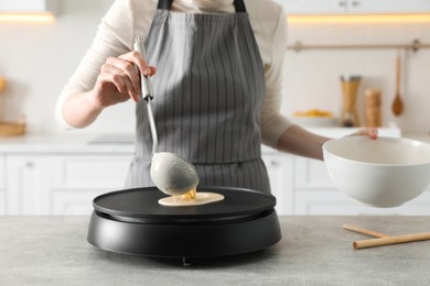 Photo of Woman cooking delicious crepe on electric pancake maker in kitchen, closeup