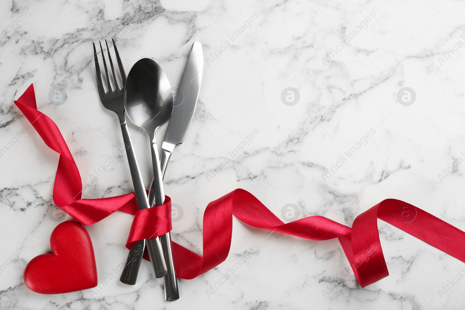 Photo of Cutlery set and red ribbon on white marble  background, flat lay with space for text. Valentine's Day dinner