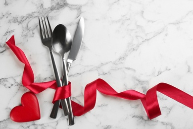 Photo of Cutlery set and red ribbon on white marble  background, flat lay with space for text. Valentine's Day dinner