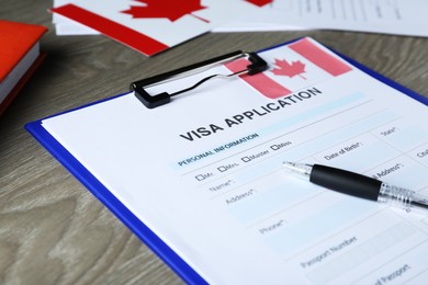 Visa application form for immigration to Canada and pen on wooden table, closeup