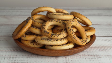 Photo of Plate with delicious ring shaped Sushki (dry bagels) on white wooden table, closeup