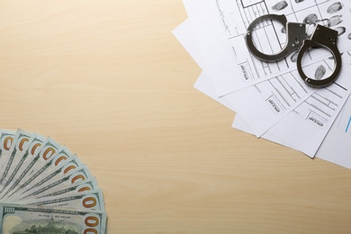 Money, handcuffs and fingerprint record sheets on wooden background, top view with space for text. Criminal investigation