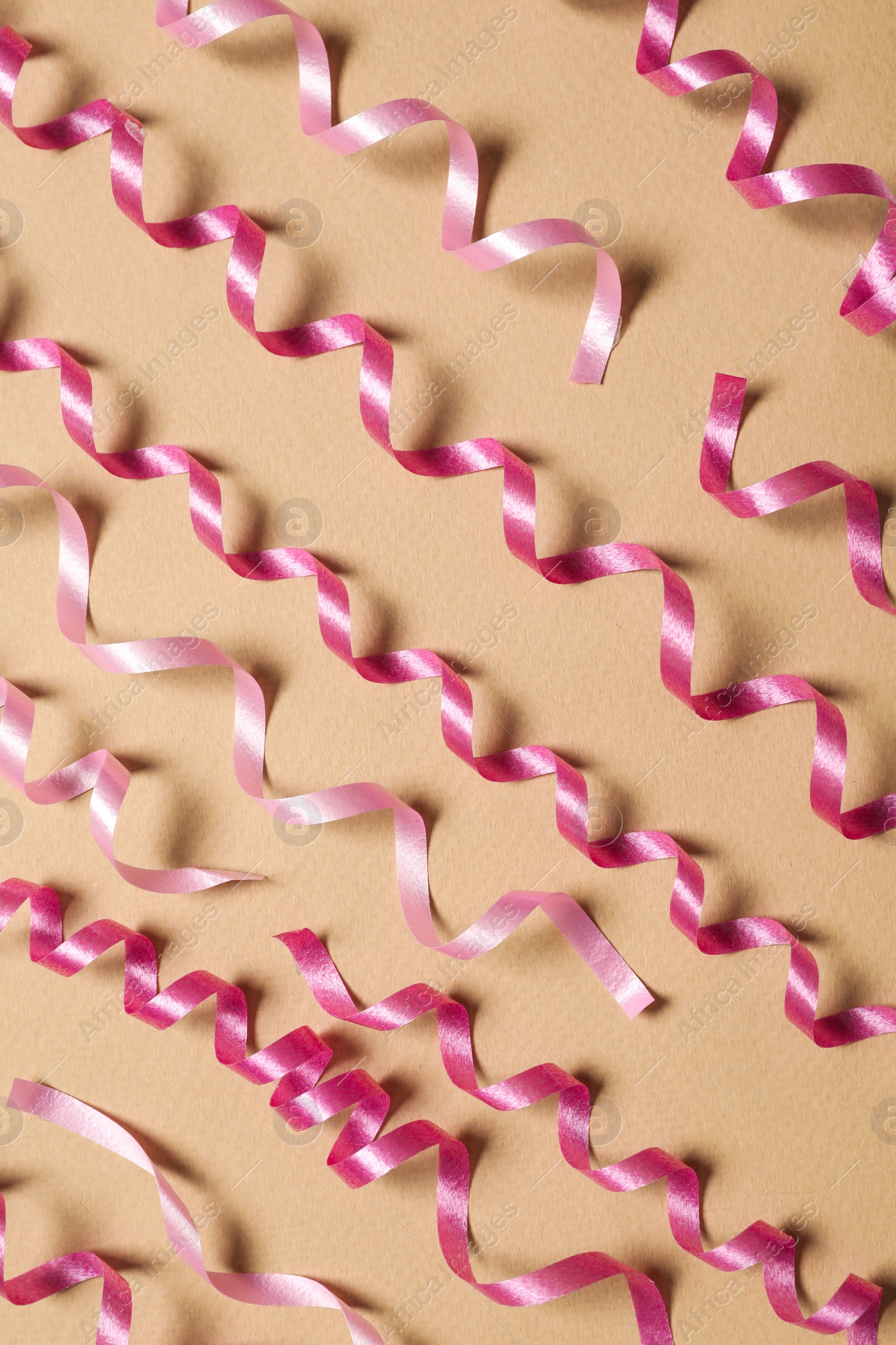 Photo of Shiny pink serpentine streamers on beige background, flat lay