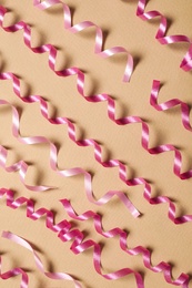 Photo of Shiny pink serpentine streamers on beige background, flat lay