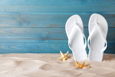 Stylish flip flops and starfish on sand near blue wooden wall, space for text