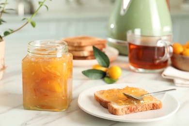 Photo of Delicious kumquat jam and sandwich on white marble table