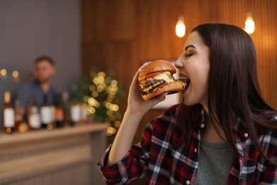 Young woman eating tasty burger in cafe