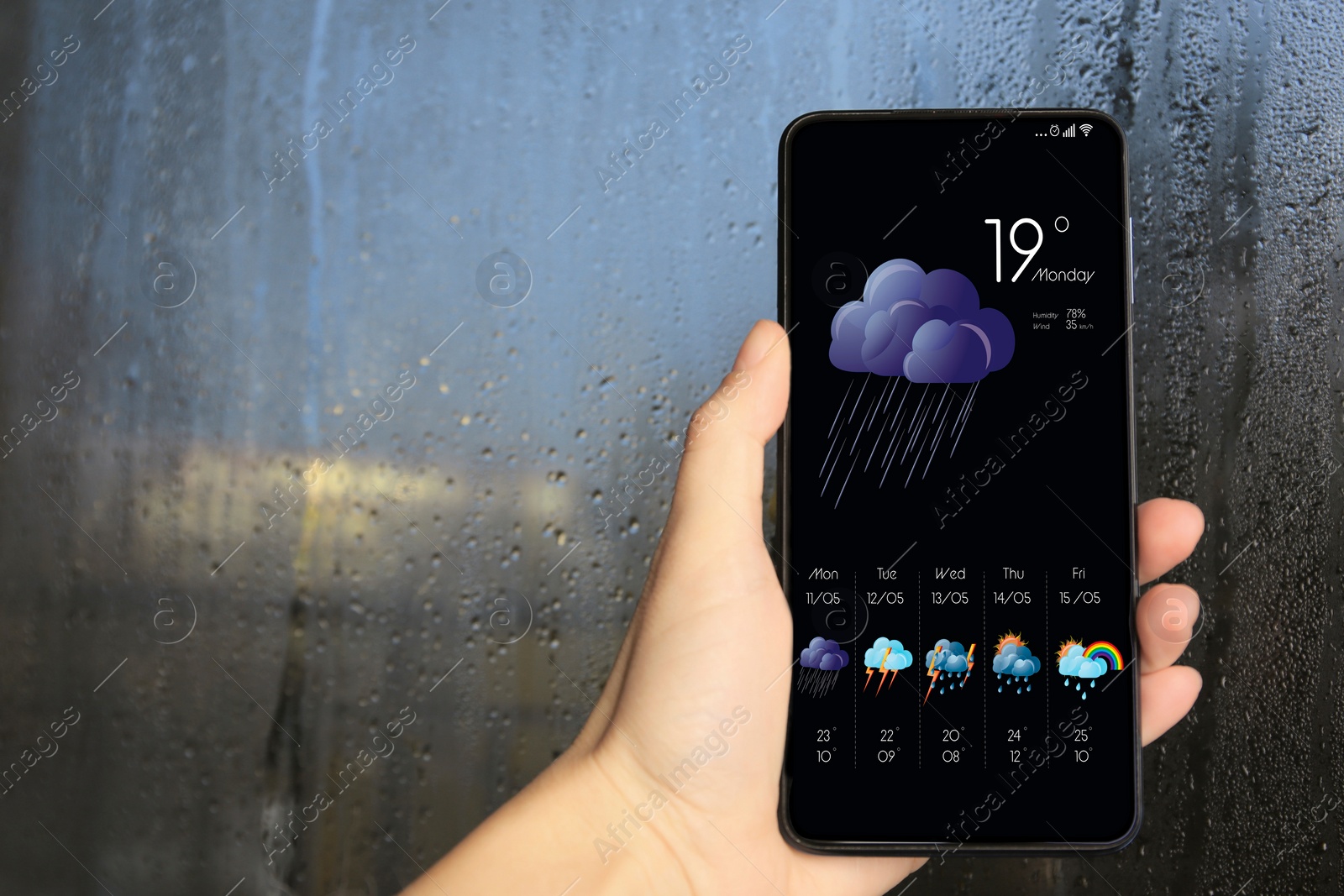 Image of Woman checking weather using app on smartphone near wet window, closeup. Data, cloud with rain and other illustrations on screen
