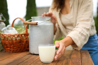 Photo of Woman taking glass with fresh milk at wooden table outdoors, closeup