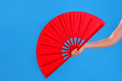 Woman holding red hand fan on light blue background, closeup