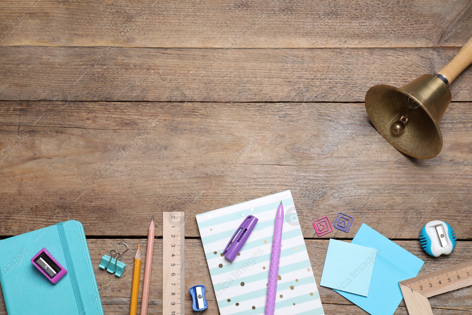 Photo of Different stationery and school bell on wooden background, flat lay. Space for text