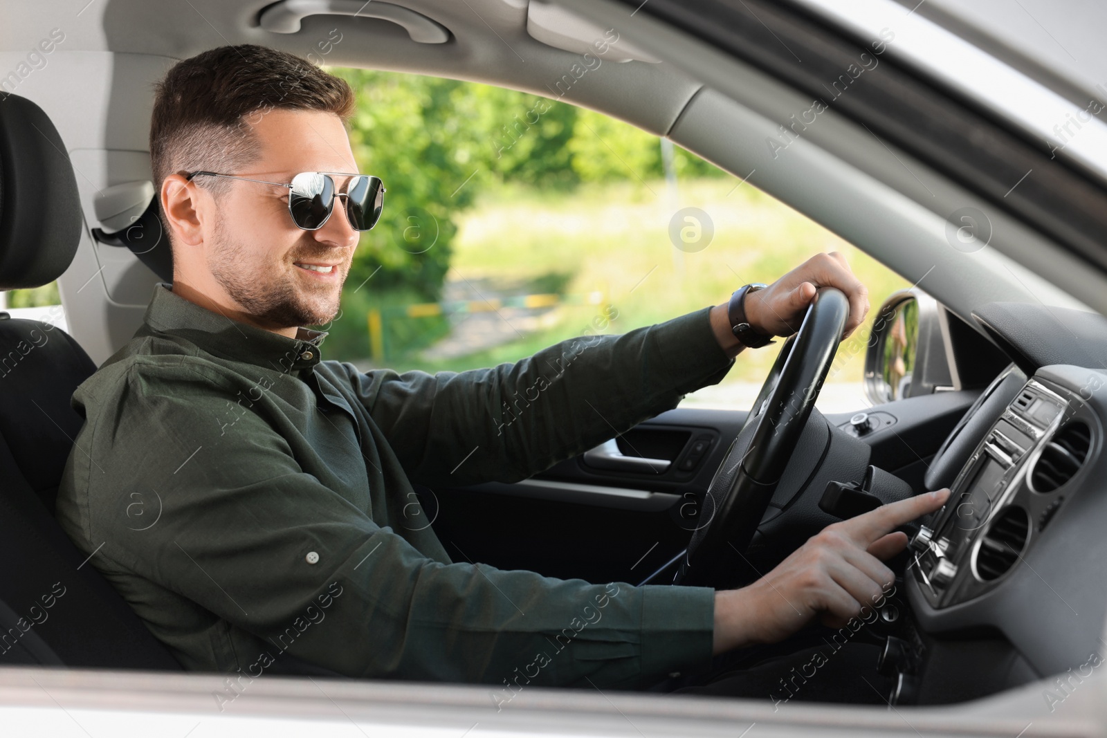 Photo of Choosing favorite radio. Man with sunglasses pressing button on vehicle audio in car