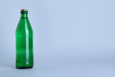 Glass bottle with water on light grey background, space for text