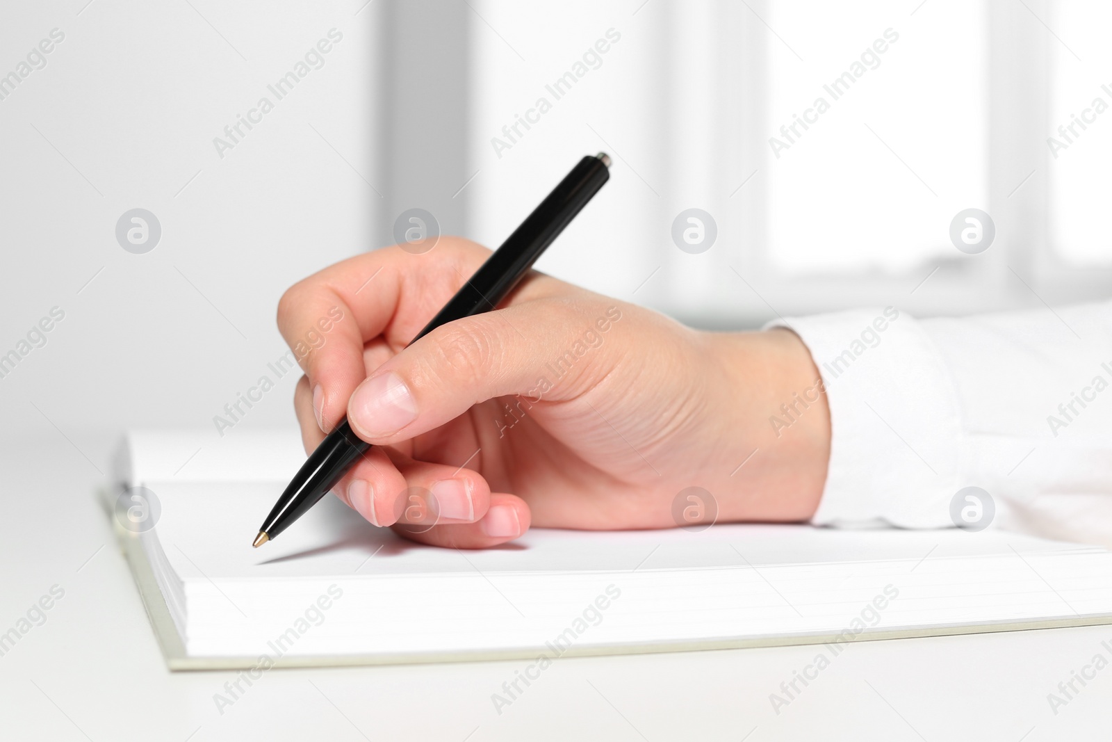 Photo of Woman writing in notebook at white table in office, closeup