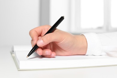 Photo of Woman writing in notebook at white table in office, closeup