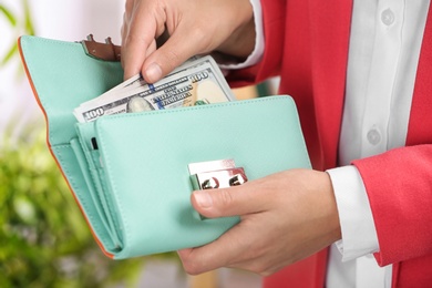 Photo of Woman taking out cash from stylish wallet on blurred background, closeup