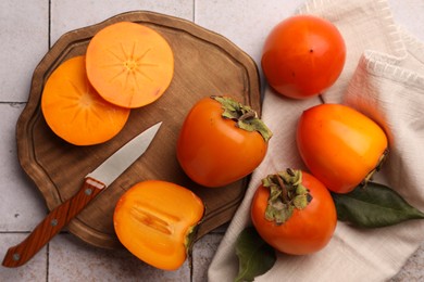 Photo of Delicious ripe juicy persimmons and knife on tiled surface