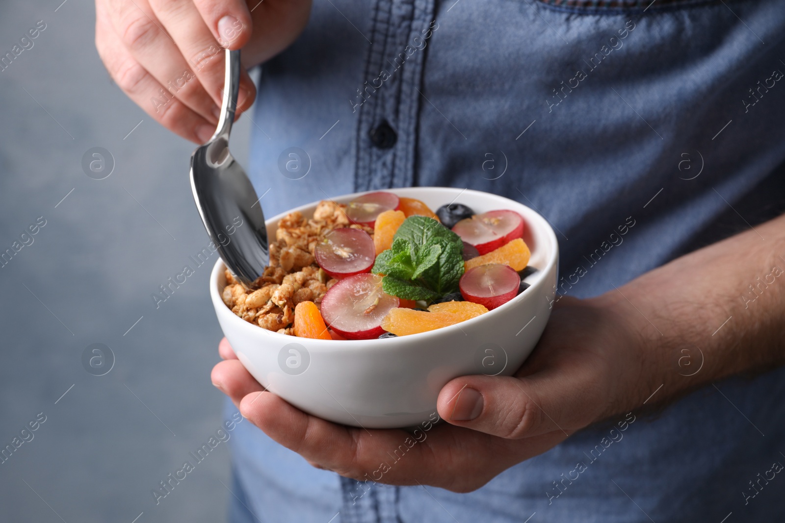 Photo of Man eating delicious granola with fruits, closeup