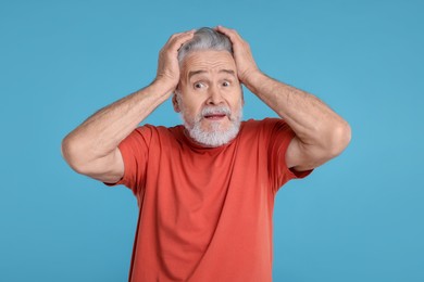 Portrait of surprised senior man on light blue background