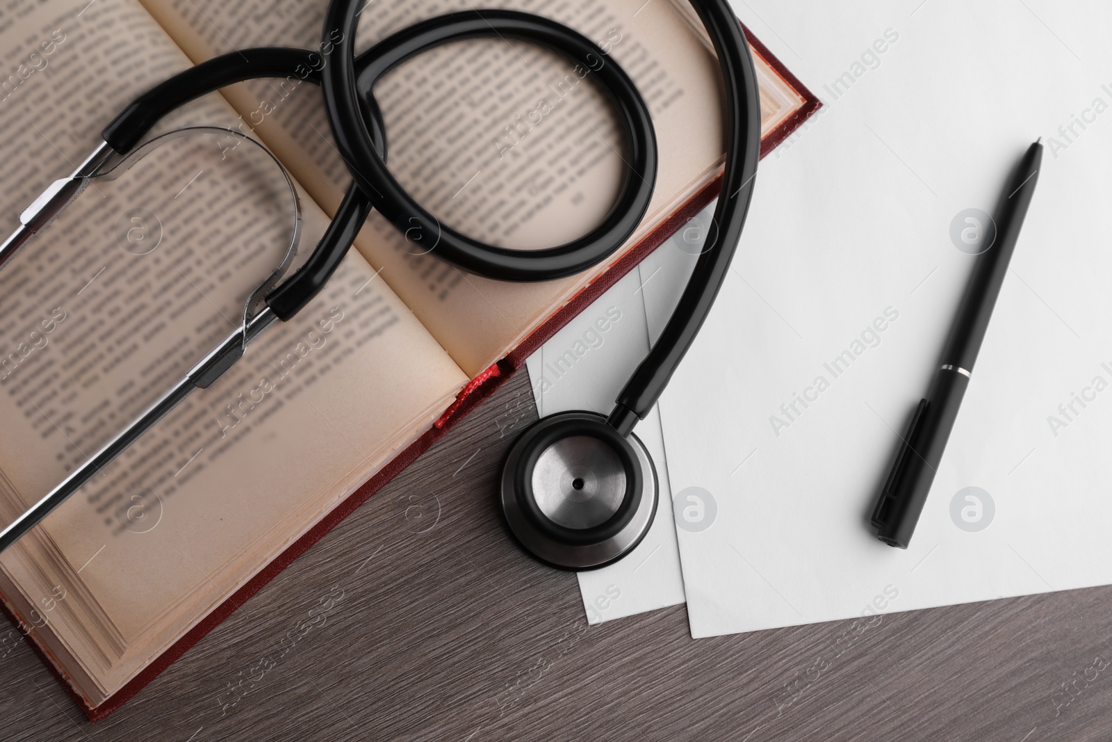 Photo of Book, stethoscope, pen and paper on wooden table, flat lay. Medical education