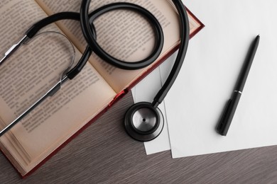 Photo of Book, stethoscope, pen and paper on wooden table, flat lay. Medical education
