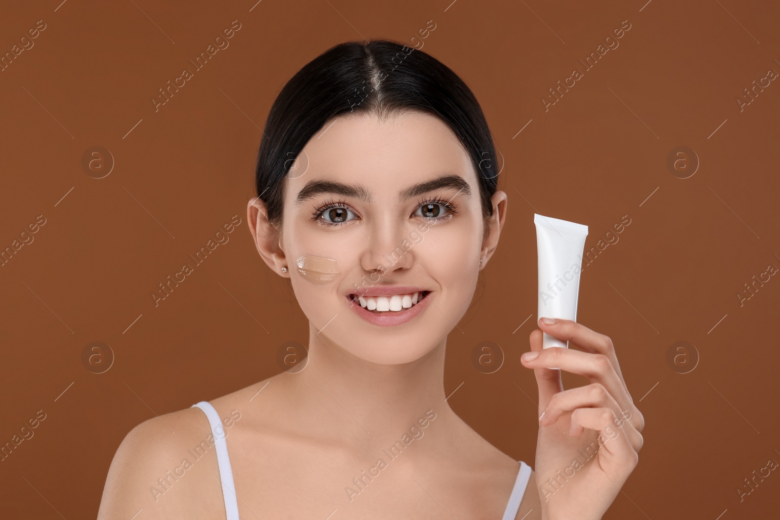 Photo of Teenage girl holding tube with foundation on brown background