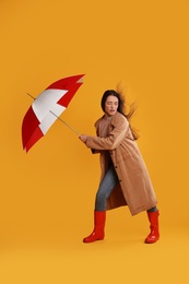 Emotional woman with umbrella caught in gust of wind on yellow background