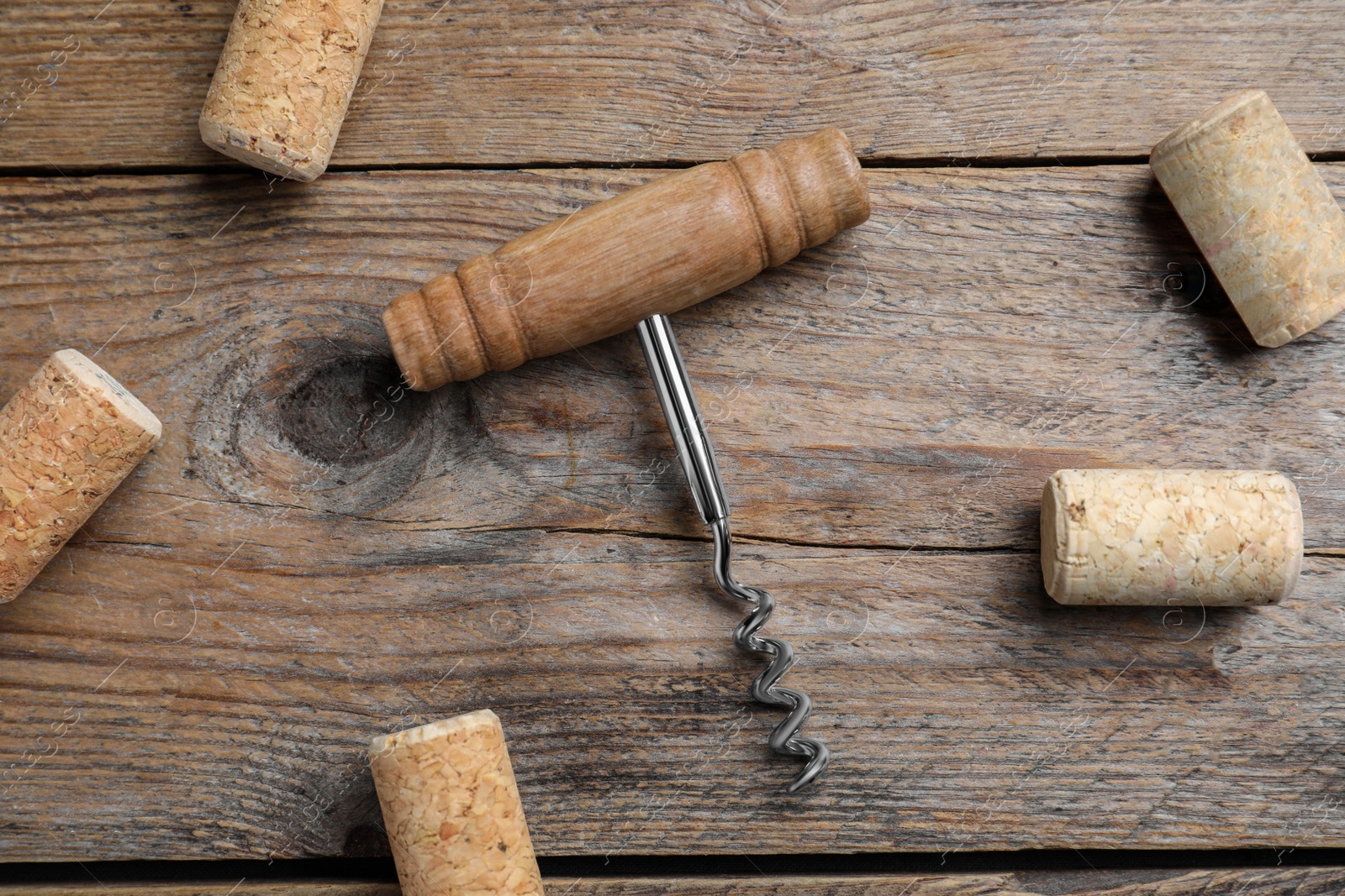 Photo of Corkscrew and wine corks on wooden table, flat lay