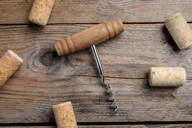Photo of Corkscrew and wine corks on wooden table, flat lay