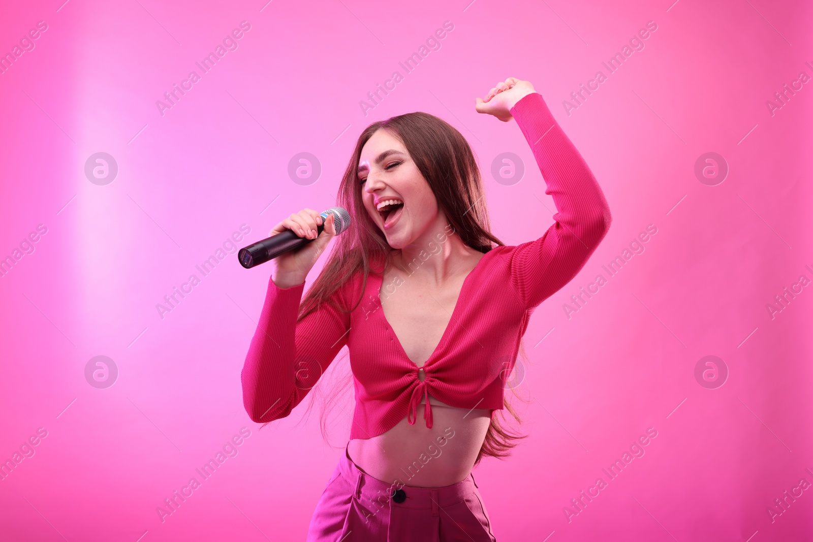 Photo of Emotional woman with microphone singing on pink background