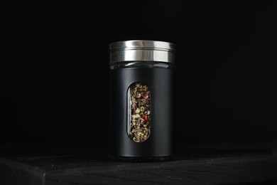 Photo of Pepper shaker on wooden board against black background