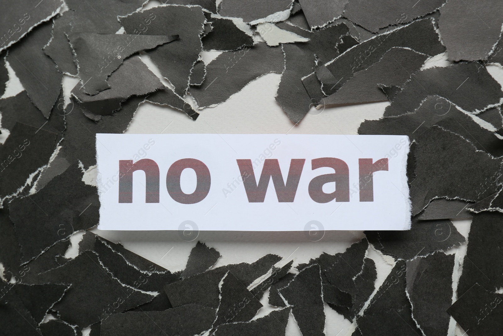 Photo of Words No War and pieces of torn black paper on white background, flat lay