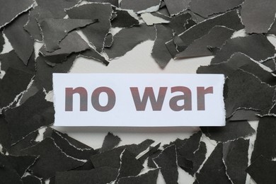Photo of Words No War and pieces of torn black paper on white background, flat lay