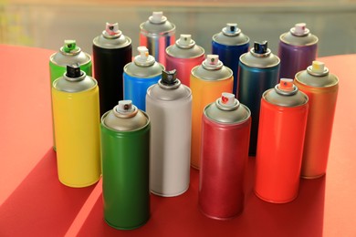 Cans of different graffiti spray paints on red table near window