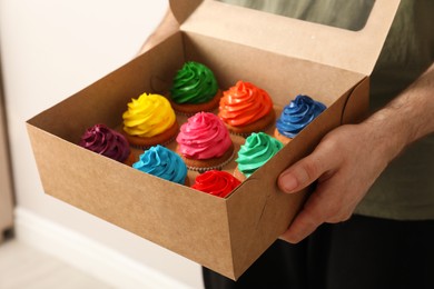 Man holding box with delicious colorful cupcakes indoors, closeup