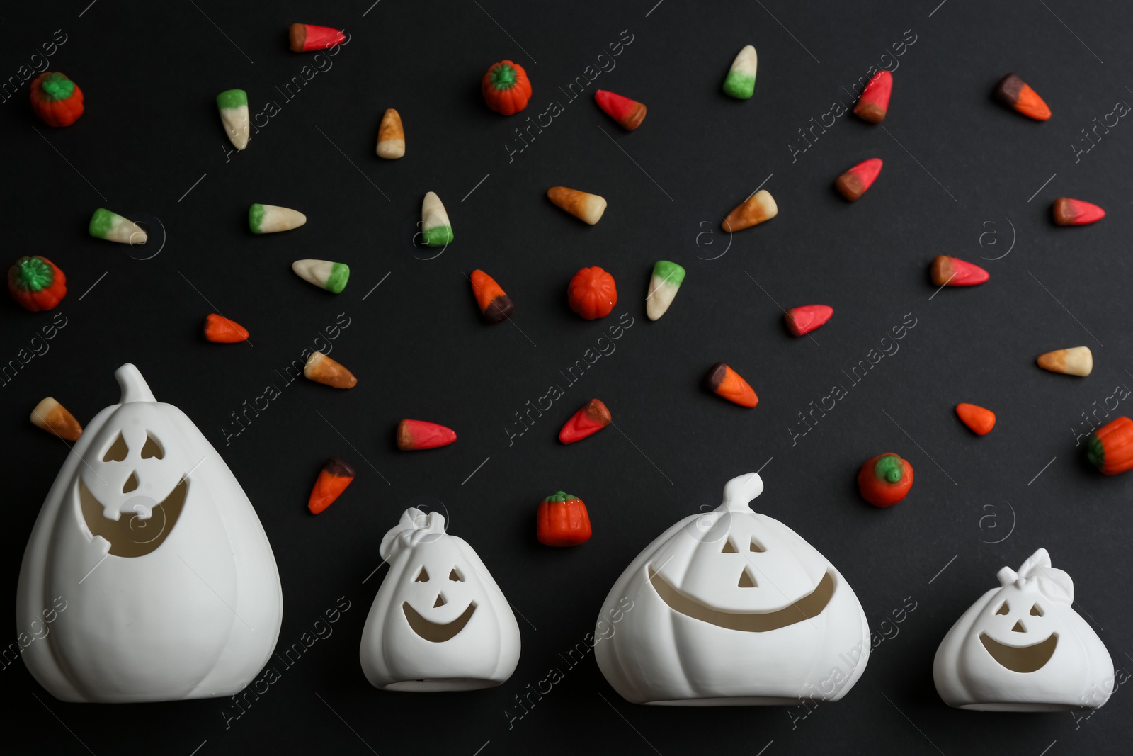 Image of White pumpkin shaped candle holders and jelly candies on black background, flat lay. Halloween decoration