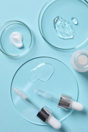 Photo of Petri dishes with samples of cosmetic serums, bottle and pipettes on light blue background, flat lay