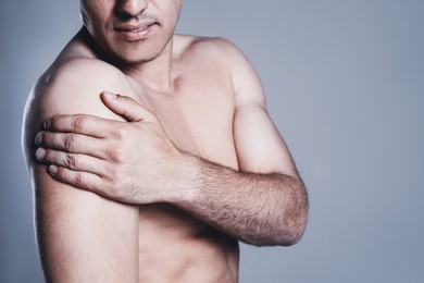 Man suffering from shoulder pain on grey background, closeup