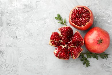 Fresh pomegranates and green leaves on grey textured table, flat lay. Space for text