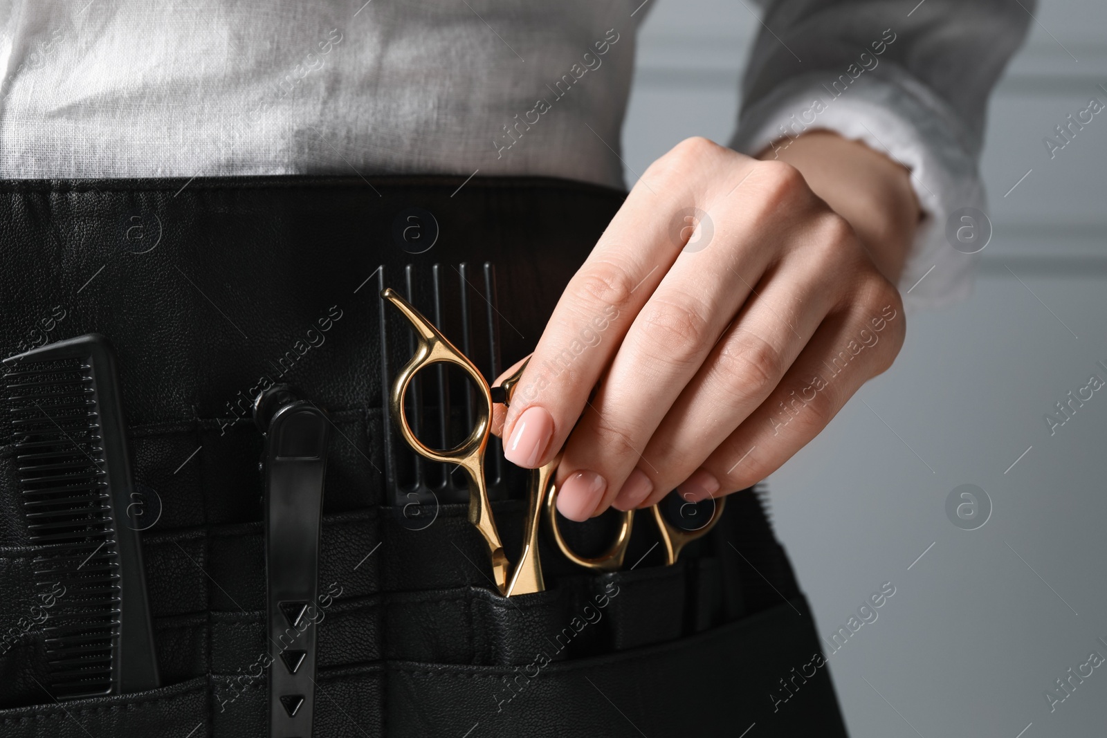 Photo of Hairstylist with professional tools in waist pouch near grey wall, closeup