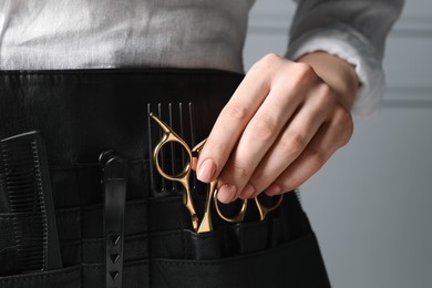 Photo of Hairstylist with professional tools in waist pouch near grey wall, closeup