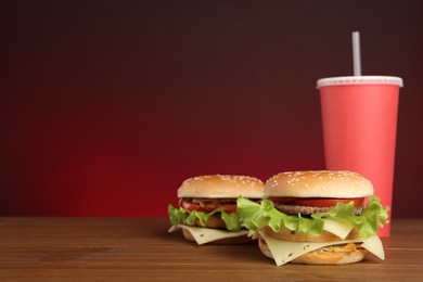 Delicious burgers and drink on wooden table against red background, space for text. Fast food menu