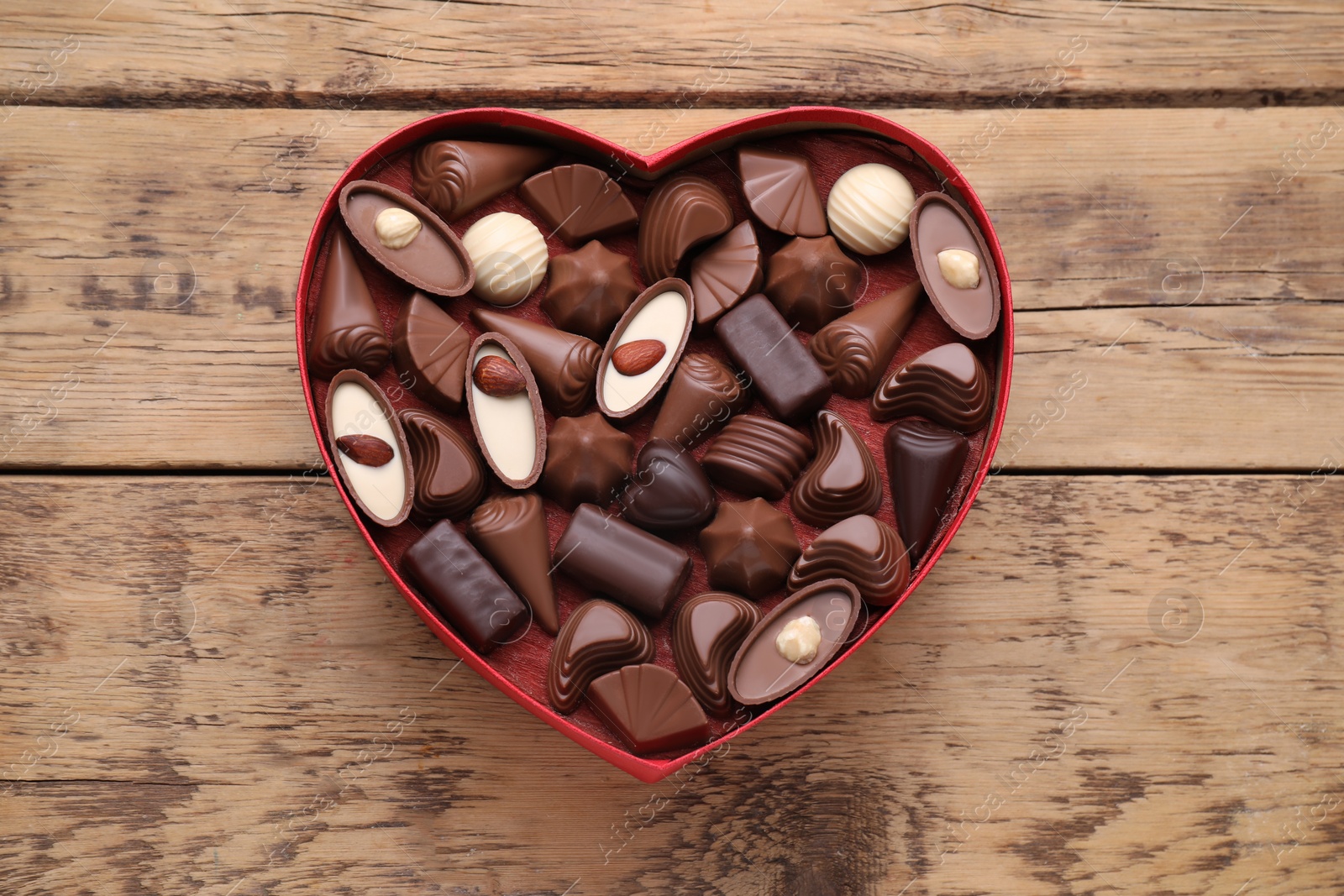 Photo of Heart shaped box with delicious chocolate candies on wooden table, top view