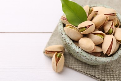 Photo of Delicious pistachios in bowl on white table, closeup. Space for text