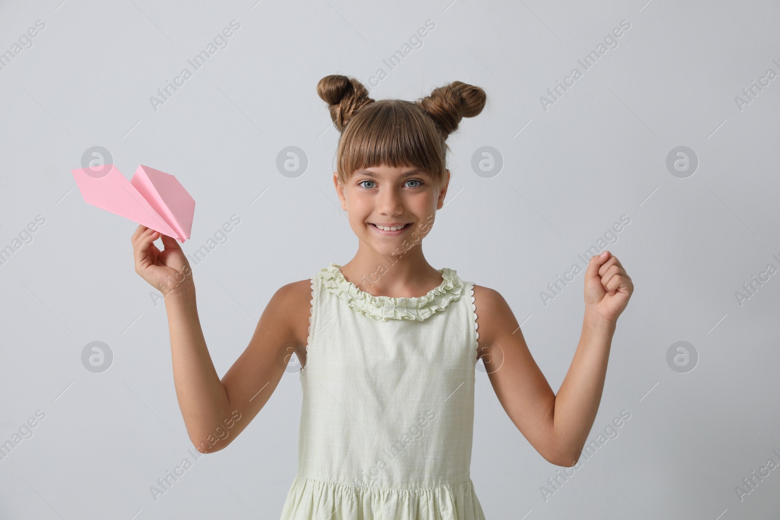 Photo of Cute little girl playing with paper plane on light grey background