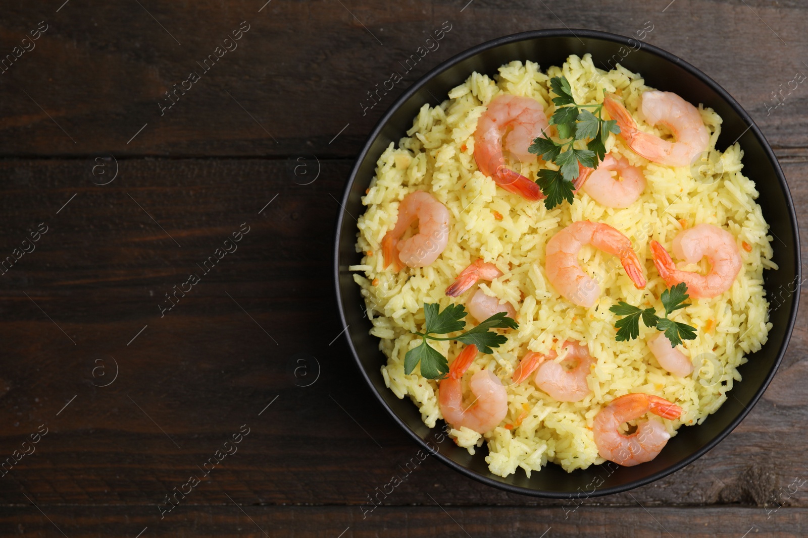 Photo of Delicious risotto with shrimps and parsley in bowl on wooden table, top view. Space for text