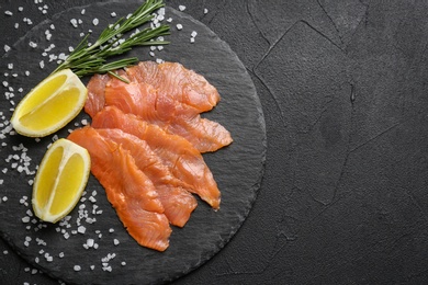 Photo of Slate plate with fresh sliced salmon fillet, rosemary and lemon on dark background, top view