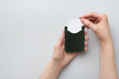 Woman holding business card holder with blank cards on light grey background, top view. Space for text