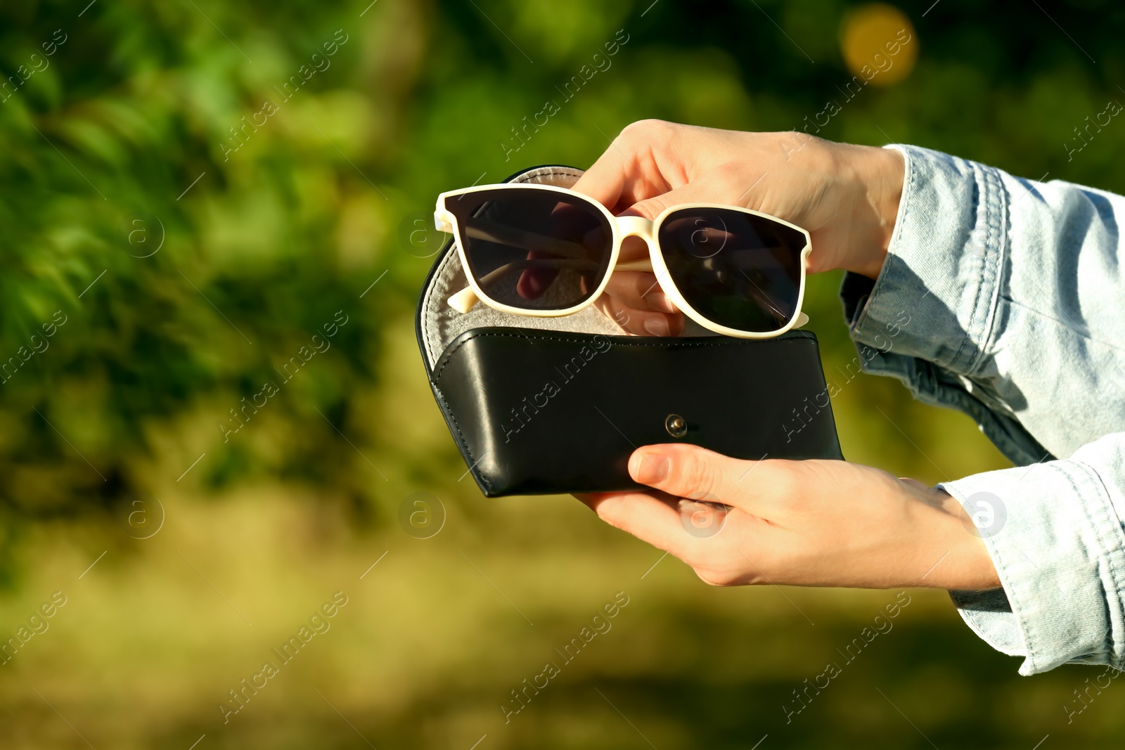 Photo of Woman holding sunglasses and case outdoors on sunny day, closeup. Space for text